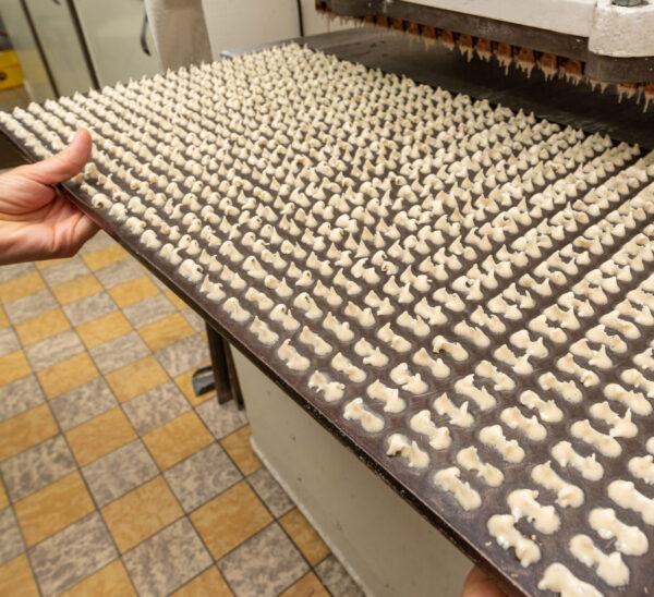 Hand hält ein Blech mit hunderten frisch dressierten Wibele-Teigtupfen in der Backstube